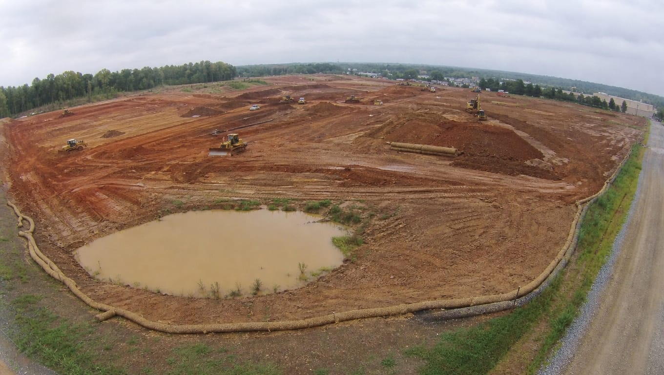 Mass grading construction site with sediment basin, perimeter controls, and exposed cut-fill slopes during maximum earth disturbance phase